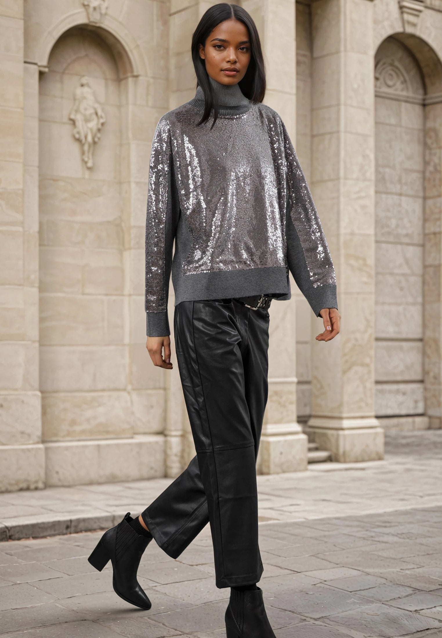Woman wearing a silver sequin sweater and black pants in front of a stone building.